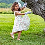 child, girl, dress, gloves, tree, grass, outdoor, nature, field, mountain, flower_pattern, curly_hair, pose, smile, footwear, greenery, playful, young, daylight, scenic