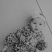 Jade is registered to the contest to win money with this photo: baby, infant, child, headband, floral_clothing, floor, portrait, black_and_white, cute, wide_eyes, pursed_lips, hand, foot, indoor, expression, head, person, young, casual, lying_down