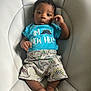 Zakari joined the competition — help win amazing prizes! baby, infant, child, blue_shirt, dinosaur_print, shorts, feet, curly_hair, chair, seated, cute, looking_at_camera, indoor, soft_furniture, clothing, new_here_text, skin, portrait, young_child, comfortable