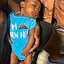 Zakari joined the competition — help win amazing prizes! baby, infant, child, onesie, blue_clothing, dinosaur_print, hand, adult, floor, blanket, footwear, indoor, skin, legs, toes, person, holding, relaxed, sleepy, casual