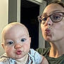 Emilia is registered to the contest to win money with this photo: baby, woman, glasses, selfie, puckered_lips, indoor, doorway, blue_eyes, short_hair, casual_clothing, child, person, skin, face, portrait, expression, holding, light, blur, close_up