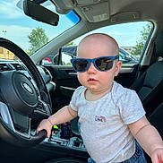 Emilia joined the competition — help win amazing prizes! baby, child, sunglasses, car_interior, steering_wheel, seat, clothing, toddler, summer, daylight, window, sky, dashboard, cute, portrait, person, vehicle, seatbelt, casual, blue