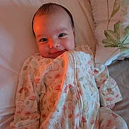 Mia joined the competition — help win amazing prizes! baby, infant, smile, onesie, bed, pillow, sleepwear, cute, child, face, cozy, indoor, soft, happy, newborn, person, lying_down, warm_light, animal_print, comfort