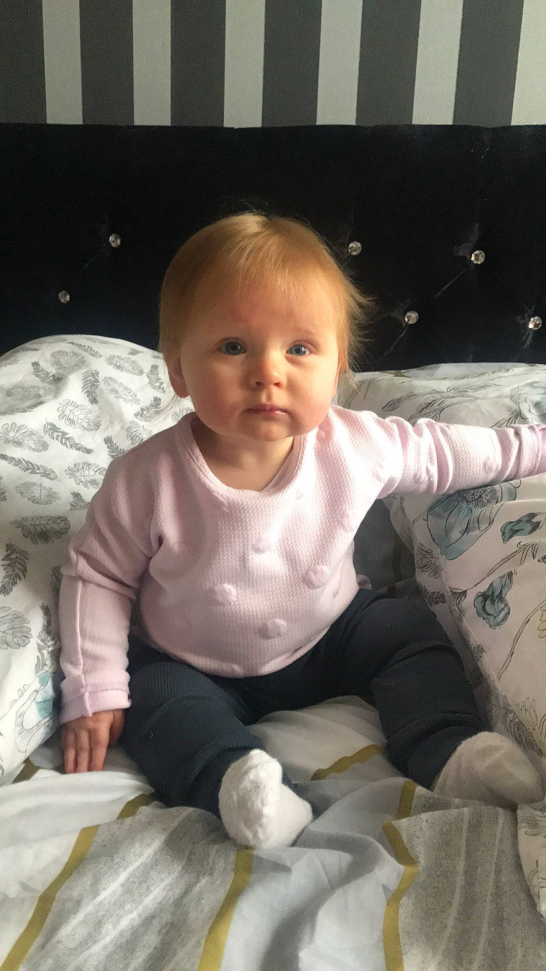 Josie is registered to the contest to win money with this photo: baby, baby_toddler_clothing, cheek, child, comfort, facial_expression, finger, hairstyle, human_body, iris, leg, linens, pattern, person, sitting, skin, sleeve, sock, standing, t_shirt