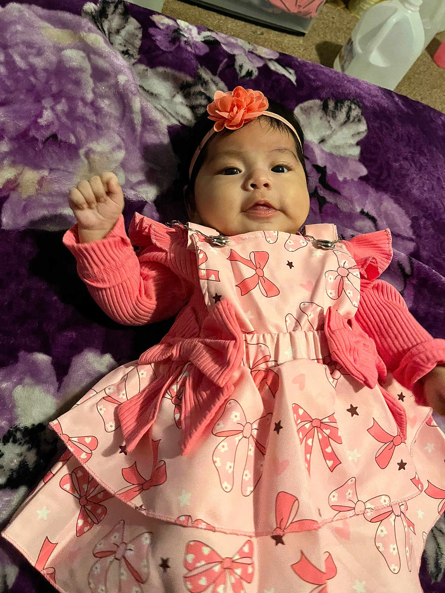 Melani joined the competition — help win amazing prizes! baby, infant, child, pink_dress, headband, flower, blanket, purple, patterned_clothing, smiling, waving_hand, indoors, portrait, cute, happy, closeup, soft_texture, young_child, person, fashion