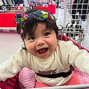 Melani joined the competition — help win amazing prizes! baby, child, smiling, shopping_cart, headband, clothing, indoor, store, retail, blanket, pink, sweater, happy, person, cute, face, curly_hair, bright_lighting, seatbelt, playful