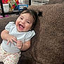 baby, child, smiling, happy, pigtails, couch, indoor, clothing, person, face, furniture, window_blinds, home, cute, portrait, sitting, young_child, fun, joy, expression