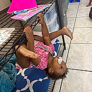 Genesis is registered to the contest to win money with this photo: toddler, child, indoor, metal_shelf, pacifier, playful, barefoot, pink_clothing, blue_rug, tile_floor, toy, hand, foot, household, storage, furniture, person, casual, child_playing, legs