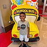child, boy, school_bus, inflatable, indoor, hallway, floor, conference_room, sign, tshirt, shorts, shoes, smiling, standing, colorful, decor, education, back_to_school, playful, person