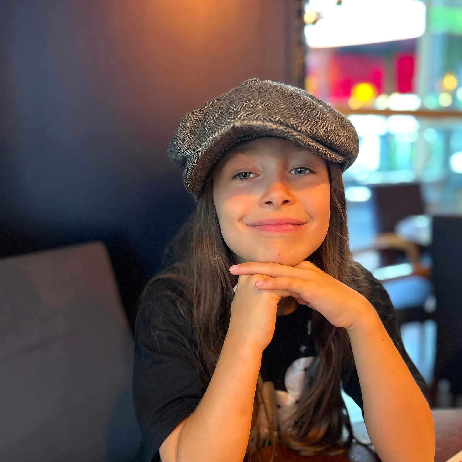 Tessa Lou a rejoint le concours — aidez-le/la à gagner de superbes lots ! blurred_background, cap, casual, child, clothing, face, fashion, hands, happy, hat, indoor, long_hair, person, portrait, restaurant, seated, smile, table, wood, young