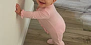 Emma joined the competition — help win amazing prizes! baby, child, pink_onesie, smiling, standing, wooden_floor, indoor, wall, baby_swing, toy, footwear, cute, happy, person, infant, home, flooring, looking_at_camera, small_toy, balance