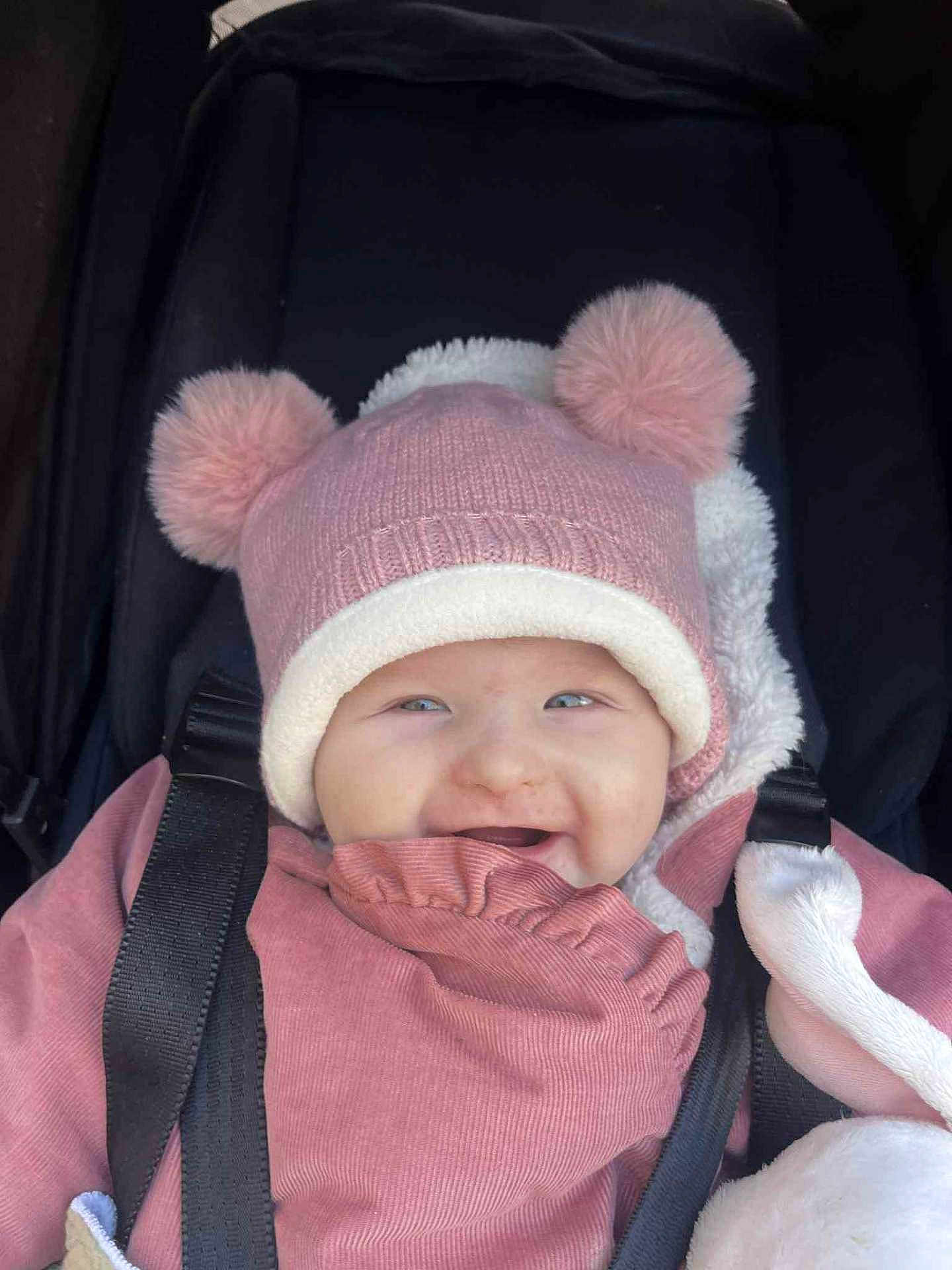 Amélia participe au concours pour gagner de l'argent avec cette photo : baby, child, smiling, pink_hat, pom_poms, stroller, cozy_clothing, happy, infant, bundle, cute, portrait, face, baby_clothes, warm, seatbelt, outdoor, closeup, person, headwear