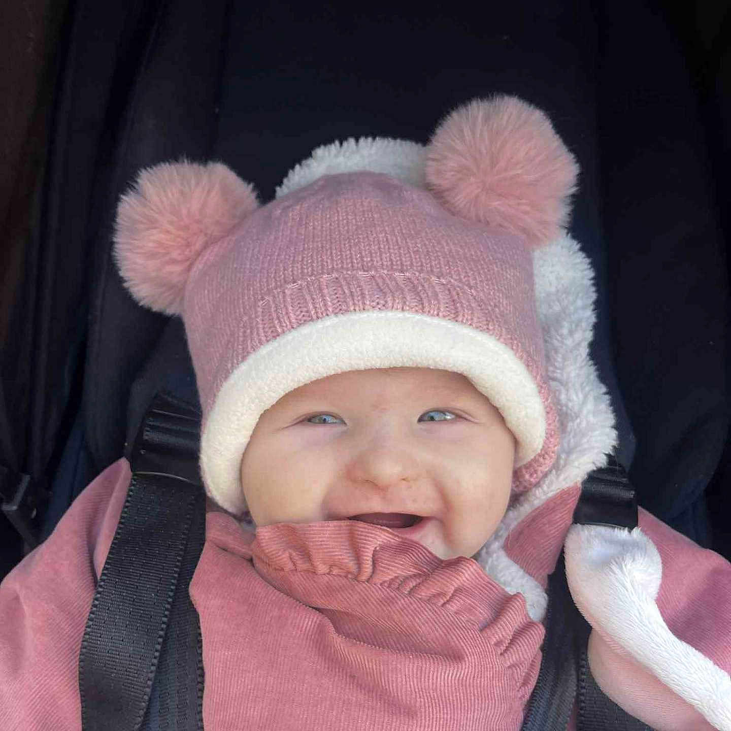 Amélia participe au concours pour gagner de l'argent avec cette photo : baby, baby_clothing, bundle_up, child, cute, face, happy, headwear, infant, jacket, outdoor, person, pink_hat, pom_poms, portrait, seat_belt, smiling, stroller, warm_clothing, winter