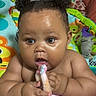 baby, child, infant, portrait, sitting, wide_eyed, curly_hair, hair_buns, bare_shoulders, bath_time, blanket, plush_toy, pink_blanket, play_mat, colorful, indoor, bedroom, close_up, happy, text_overlay