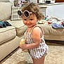 toddler, child, indoor, sunglasses, purse, carpet, couch, blanket, furniture, plaid_pillow, curly_hair, striped_clothing, barefoot, smile, person, home, living_room, cute, playful, fashion