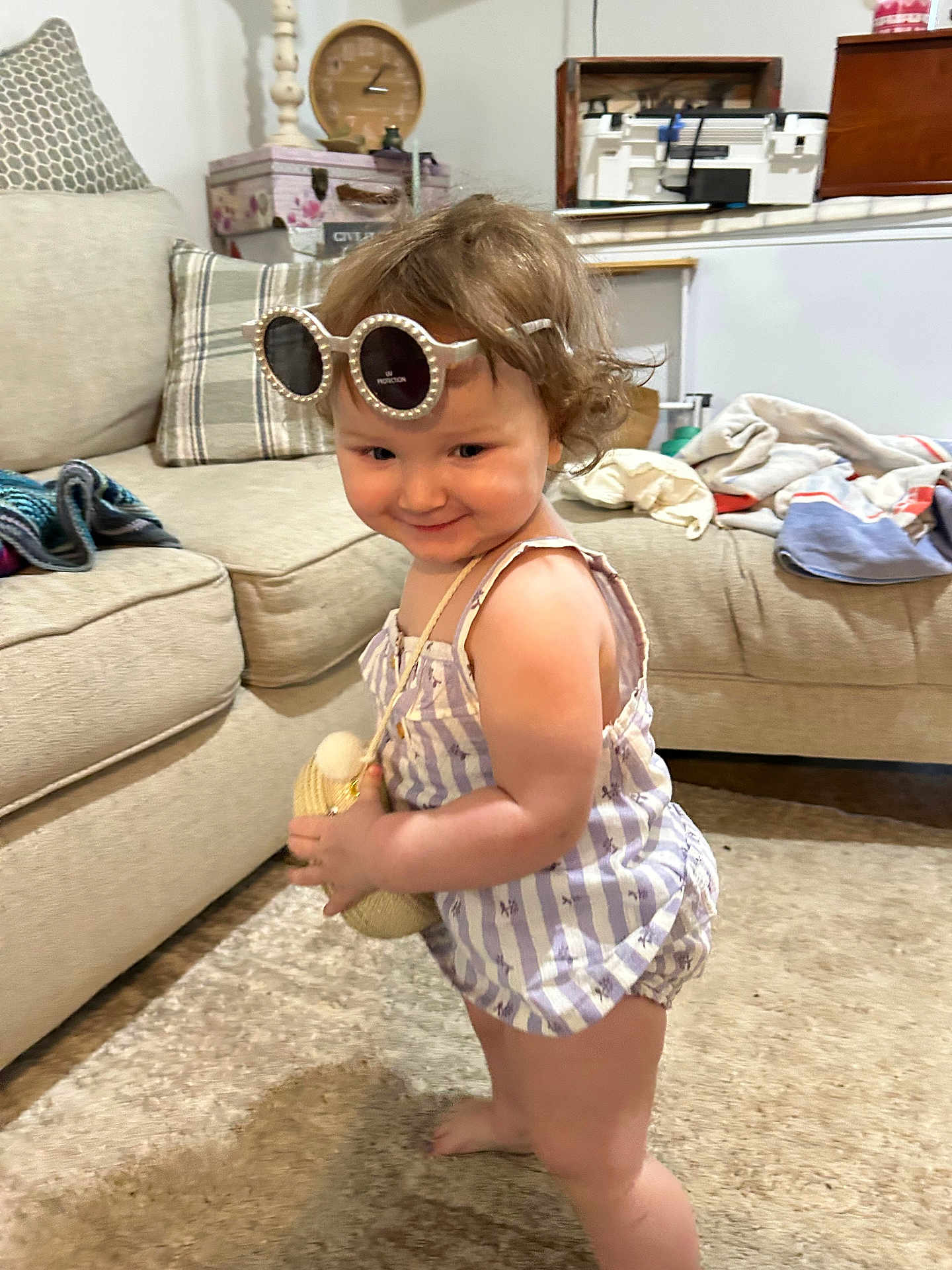 Harmony joined the competition — help win amazing prizes! toddler, child, indoor, sunglasses, purse, carpet, couch, blanket, furniture, plaid_pillow, curly_hair, striped_clothing, barefoot, smile, person, home, living_room, cute, playful, fashion