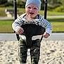baby, child, swing, playground, hat, smile, happy, outdoor, park, sand, clothing, camo_pants, sock, person, daylight, fun, joy, infant, seat, chains