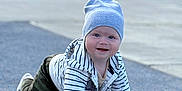 Mark is registered to the contest to win money with this photo: baby, child, crawling, beanie, striped_hoodie, blue_surface, outdoor, playground, park_bench, greenery, happy, smiling, person, casual_clothing, cute, young_child, daylight, playing, fun, headwear