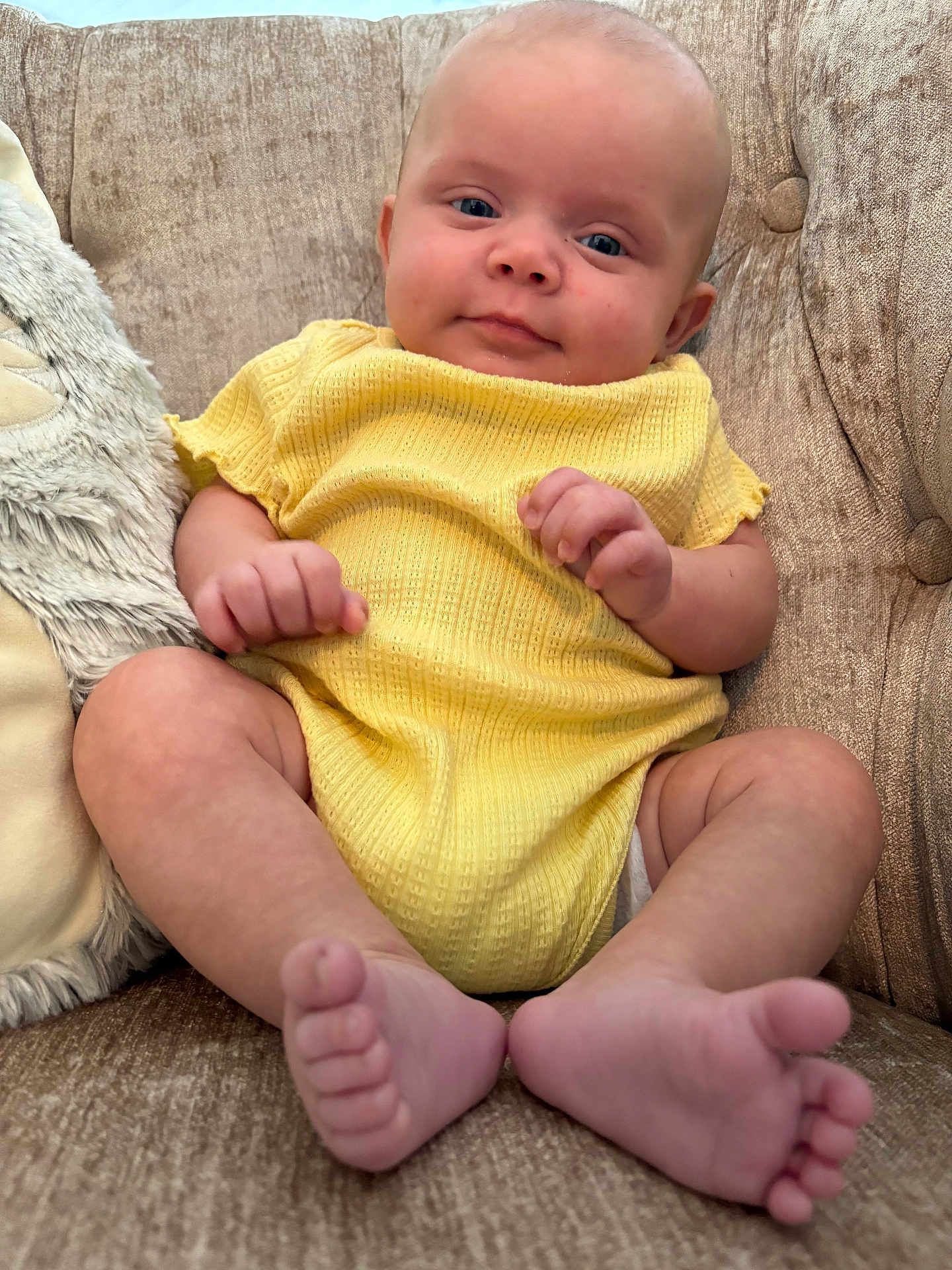 Raylynn joined the competition — help win amazing prizes! baby, infant, yellow_clothing, couch, sofa, barefoot, toes, hands, face, blue_eyes, skin, indoor, child, seated, plush_pillow, texture, relaxed, comfort, portrait, cute