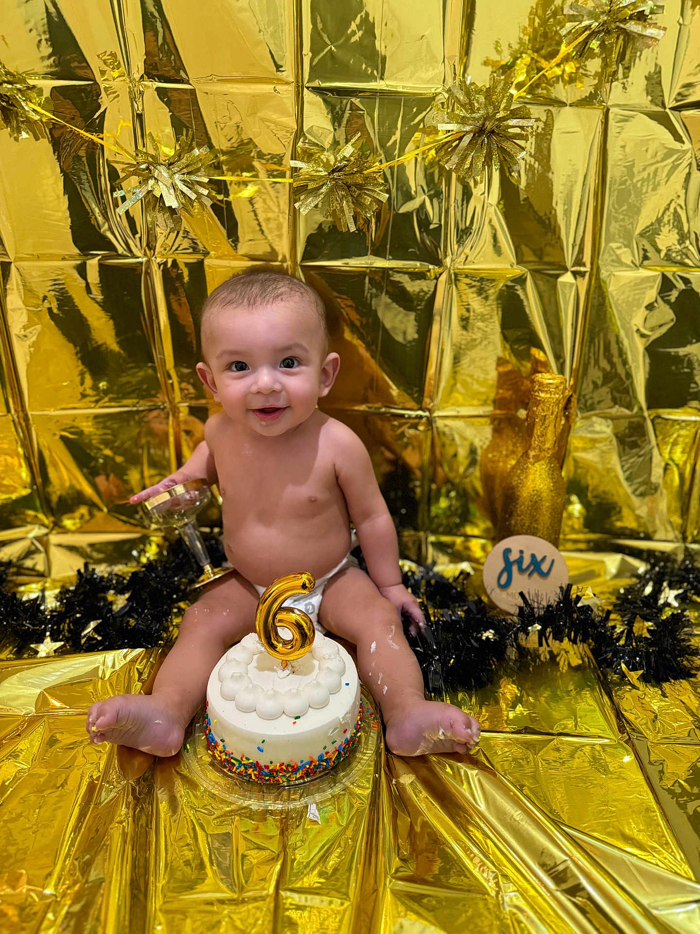 Kayden is registered to the contest to win money with this photo: baby, smile, cake, candle, party, celebration, gold, decoration, diaper, glass, background, tinsel, birthday, infant, sitting, cute, festive, happy, colorful, milestone