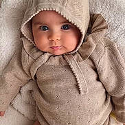 Luz participe au concours pour gagner de l'argent avec cette photo : baby, infant, hooded_clothing, knitted_outfit, beige, blanket, soft_texture, cute, portrait, lying_down, face, eyes, pout, cozy, child, warm_clothing, indoors, skin, person, young_child