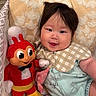 Monako is registered to the contest to win money with this photo: baby, smiling, plush_toy, pillow, bib, onesie, indoor, child, cute, soft_toy, patterned, animal_print, happy, infant, face, hand, colorful, fabric, person, portrait