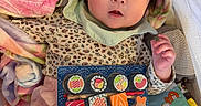 Monako is registered to the contest to win money with this photo: baby, infant, toy, blanket, colorful, face, cute, child, clothing, play, sushi_toy, pink_pants, patterned_shirt, soft_toy, bed, indoor, hand, expression, young, lying_down