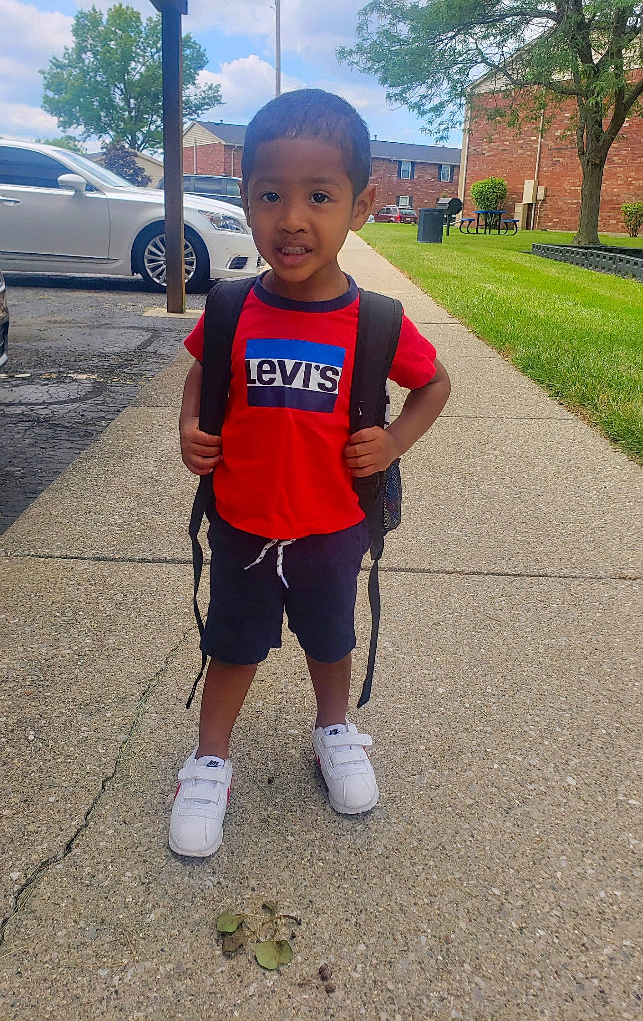 Lennox is registered to the contest to win money with this photo: asphalt, athlete, car, electric_blue, fun, person, plant, recreation, road, running, shorts, sidewalk, sky, smile, sneakers, sportswear, t_shirt, tire, toddler, tree