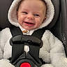 baby, child, car_seat, smile, happy, infant, white_clothing, hood, fluffy, seatbelt, indoor, cute, young_child, safety, red_button, fur_texture, portrait, headrest, baby_clothes, seat