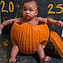 Link is registered to the contest to win money with this photo: baby, pumpkin, halloween, child, orange, face, legs, arms, black_background, paint, floor, cute, holiday, costume, celebration, indoors, person, skin, head, expression
