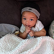 Link joined the competition — help win amazing prizes! baby, infant, child, blanket, pacifier, hat, nike, couch, dark_background, white_clothing, thumb_sucking, cute, face, eyes, hand, soft_texture, cozy, indoor, portrait, relaxed