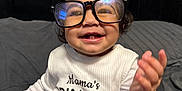 Sanaya is registered to the contest to win money with this photo: baby, child, glasses, smiling, happy, sitting, clothing, white_shirt, denim_skirt, indoor, bed, bedding, headboard, person, portrait, cute, joyful, infant, apparel, young_child