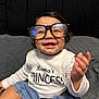 baby, child, glasses, smiling, happy, sitting, clothing, white_shirt, denim_skirt, indoor, bed, bedding, headboard, person, portrait, cute, joyful, infant, apparel, young_child