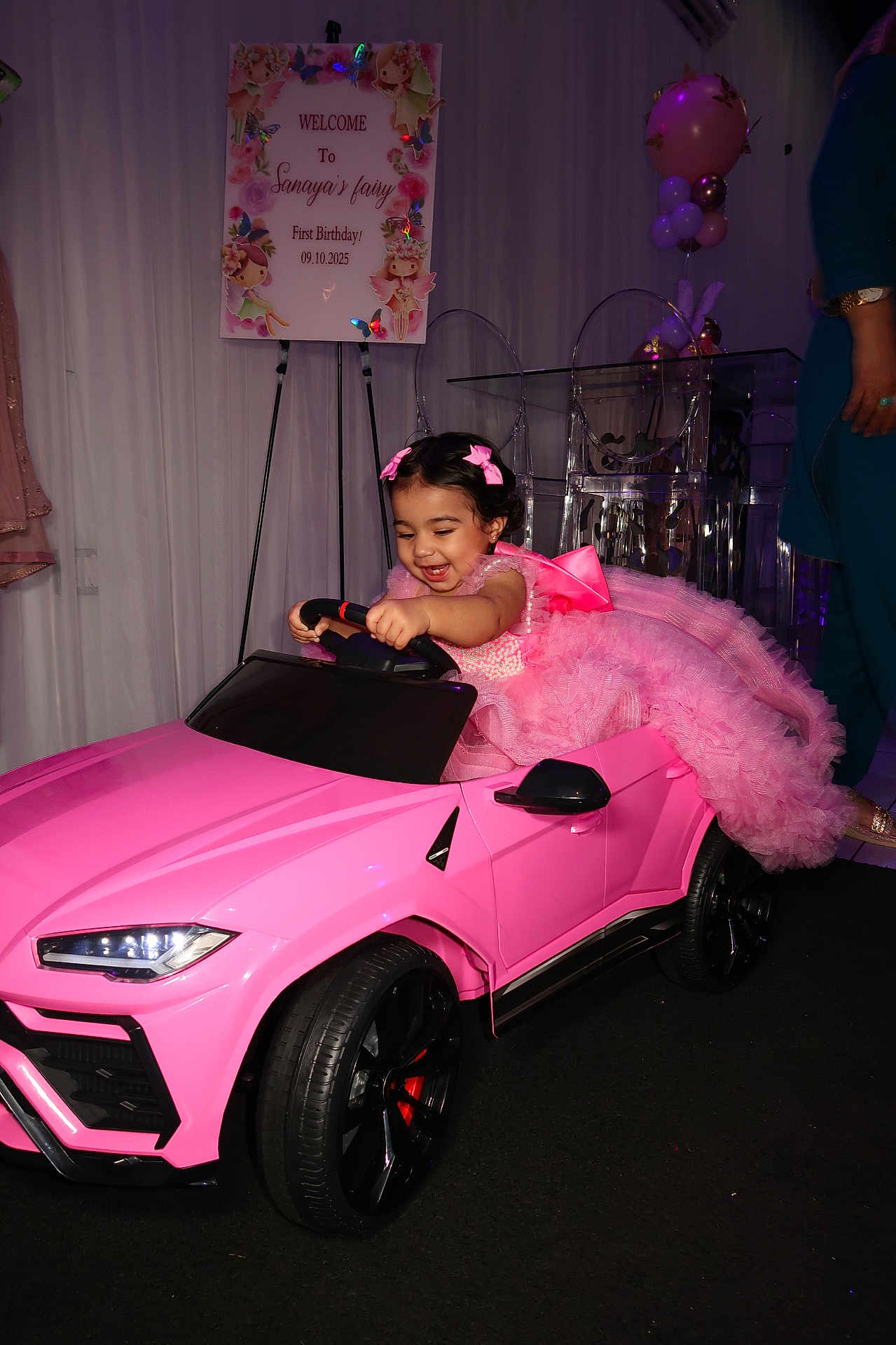 Sanaya is registered to the contest to win money with this photo: child, toddler, pink_dress, toy_car, birthday_party, balloons, celebration, smiling, indoor, steering_wheel, happy, decorations, ribbons, face, person, event, fun, joy, floor, clothing