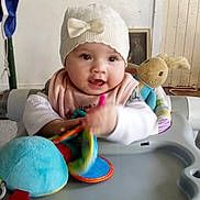 Loren Anakiwa joined the competition — help win amazing prizes! baby, child, walker, toy, plush_bunny, hat, indoor, smiling, colorful, clothing, person, face, hand, flag, wooden_panel, table, seat, infant, play, cute