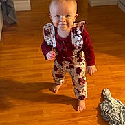 Enora is registered to the contest to win money with this photo: toddler, child, baby, floor, wooden_floor, clothing, overalls, maroon_shirt, smiling, hair, pigtails, barefoot, indoor, home, person, cute, walking, fabric, playful, young_child