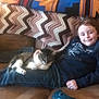 Ollie joined the competition — help win amazing prizes! boy, cat, couch, blanket, pillow, child, indoor, relaxing, smile, pet, jeans, long_sleeve_shirt, home, comfort, brown_couch, floral_pattern, striped_blanket, casual, resting, friendship