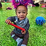 Cookie is registered to the contest to win money with this photo: baby, child, toy, headband, fuzzy, purple, red, striped_pants, pacifier, carpet, green, indoor, people, sitting, playing, smiling, happy, adult, background, casual_clothing