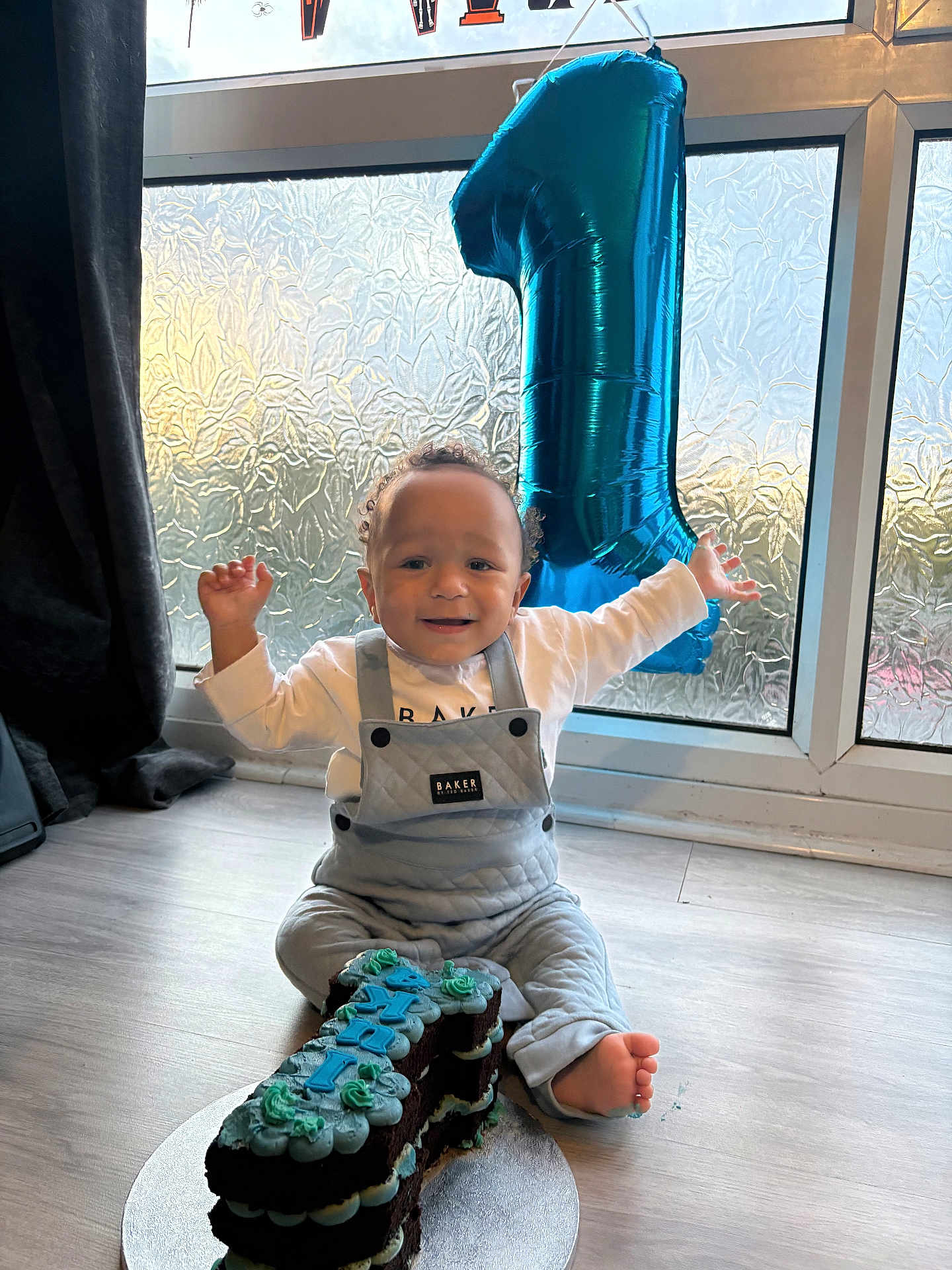 Cookie joined the competition — help win amazing prizes! baby, child, birthday, cake, number_one, balloon, celebration, smile, happy, indoor, floor, clothing, overalls, window, natural_light, curtain, foot, person, party, decorations