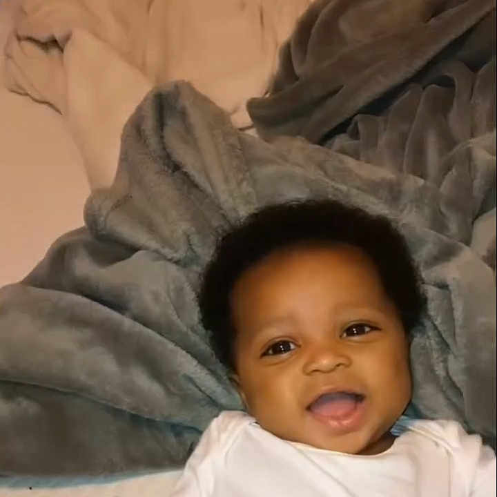 M'Kai joined the competition — help win amazing prizes! baby, blanket, child, comfort, cozy, cute, expression, face, happy, head, indoor, infant, lying_down, portrait, skin, smiling, soft_texture, warm, white_clothing, young_child