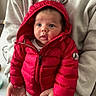 baby, child, red_jacket, hood, ears, puffy_jacket, hands, adult, sweatshirt, beige_clothing, indoor, curious, wide_eyes, portrait, person, holding, seated, warm_clothing, cute, infant