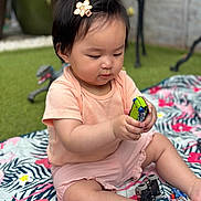 Freya is registered to the contest to win money with this photo: baby, blanket, child, colorful, cute, dinosaur_toy, focus, fun, grass, hair_clip, hand, legs, nature, outdoor, peach_clothing, playing, sitting, small_toys, summer, toy_car