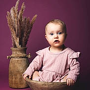 Djensy participe au concours pour gagner de l'argent avec cette photo : baby, child, curious, cute, decor, dried_grass, expression, face, indoor, infant, pampas_grass, person, pink_clothing, portrait, purple_background, sitting, soft_lighting, studio_lighting, vase, wooden_bowl