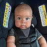 baby, child, car_seat, safety_harness, warning_label, straps, curious_eyes, tongue_out, chubby_cheeks, infant, seatbelt, cute, portrait, indoor, person, clothing, head, face, young_child, expression