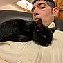 cat, black_cat, sleeping, person, indoor, lamp, chair, sweater, cozy, relaxing, furniture, wood, home, pet, resting, close_up, comfort, animal, cute, warm_lighting