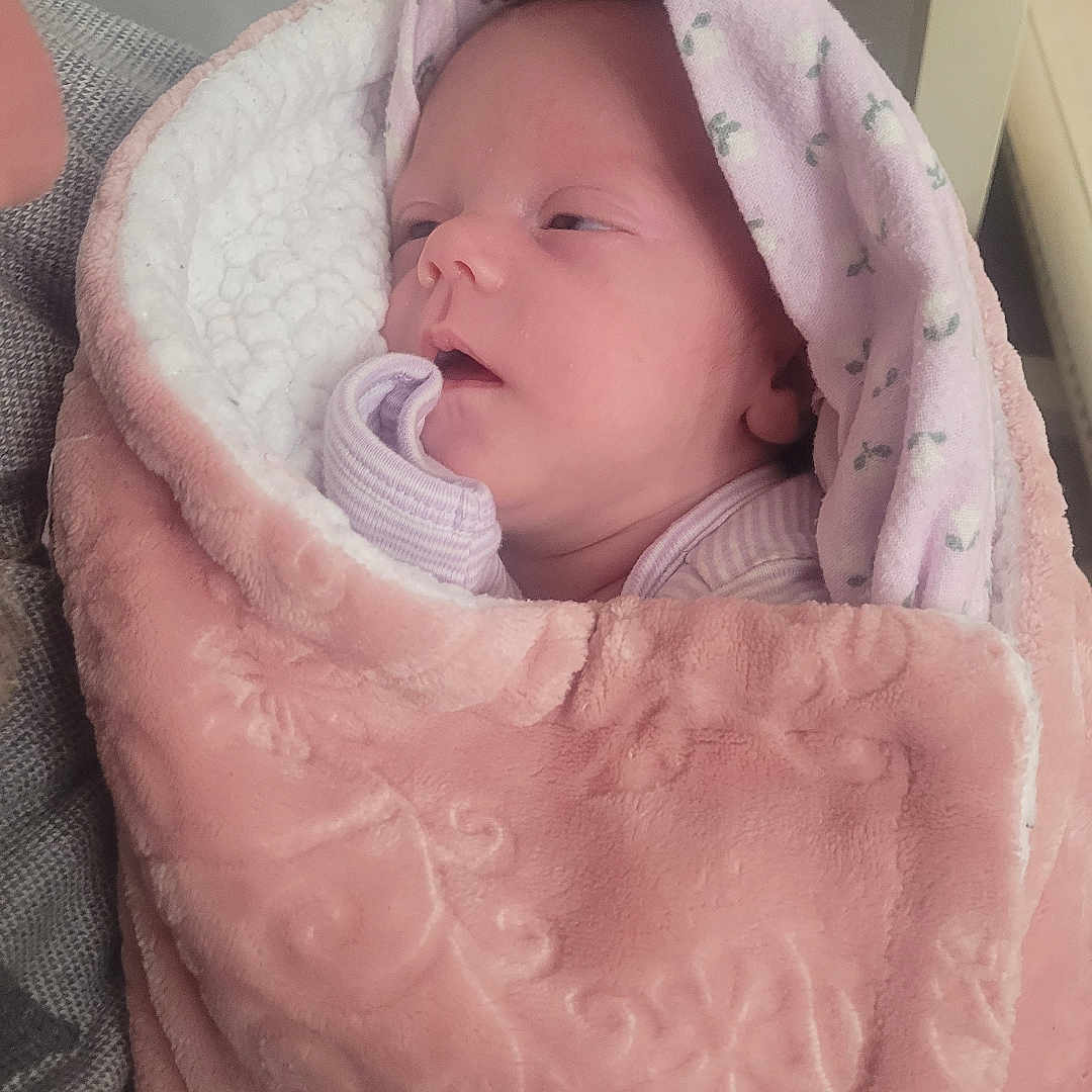 Jasmin joined the competition — help win amazing prizes! adult_arm, arm, baby, blanket, cozy, fabric, face, fleece, head, hood, indoor, infant, mouth, newborn, pattern, person, pink_blanket, portrait, sleeping, swaddle