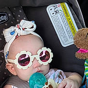 Danaerys is registered to the contest to win money with this photo: baby, car_seat, sunglasses, head_wrap, pacifier, toy, giraffe_toy, child, infant, polka_dot, fabric, cute, hand, clothing, seatbelt, accessory, portrait, close_up, indoor, safe