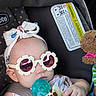 baby, car_seat, sunglasses, head_wrap, pacifier, toy, giraffe_toy, child, infant, polka_dot, fabric, cute, hand, clothing, seatbelt, accessory, portrait, close_up, indoor, safe