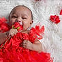 baby, child, red_dress, flower, rose, fluffy_surface, happy, smiling, portrait, cute, tulle, infant, hand, face, lying_down, celebration, bright_colors, soft_texture, closeup, adorable