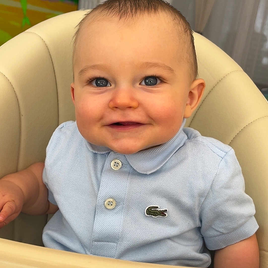 Liam participe au concours pour gagner de l'argent avec cette photo : baby, blue_eyes, child, clothing, crocodile_logo, curtains, cute, face, happy, head, high_chair, indoor, infant, person, polo_shirt, seated, short_sleeves, smiling, television, young